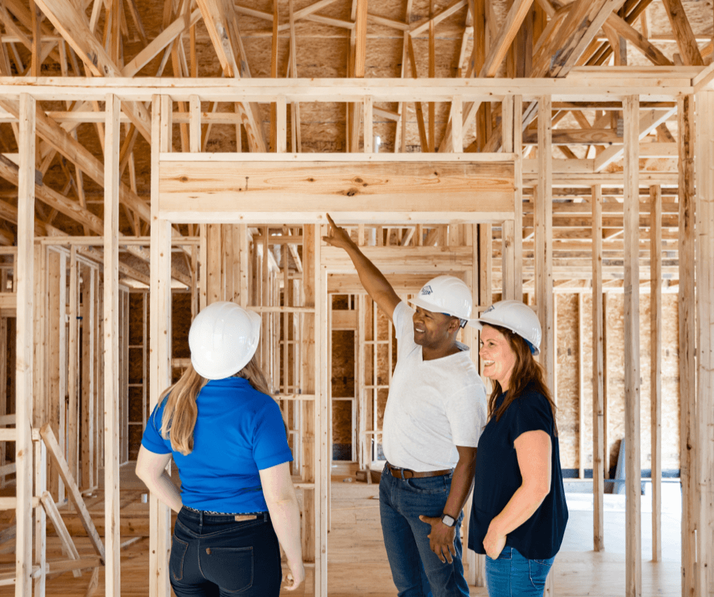Three Clayton team members in hard hats inspecting the wood framing inside a new home under construction.