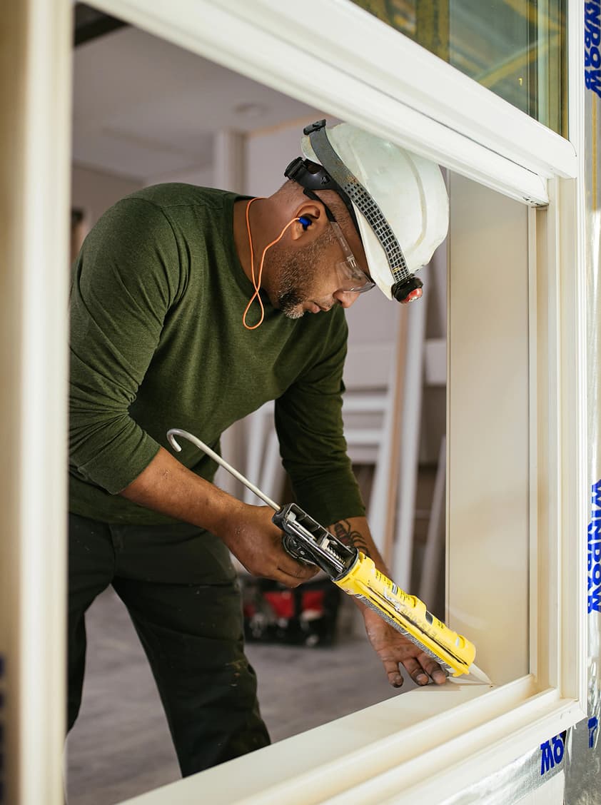 A builder caulks a seal in a window to ensure the home is sealed and energy efficient.