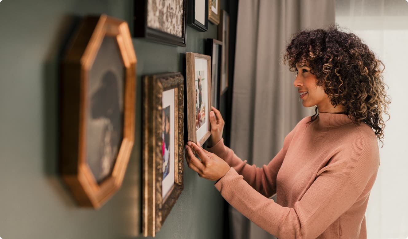A woman hangs pictures in frames on a green wall inside her modern manufactured home.