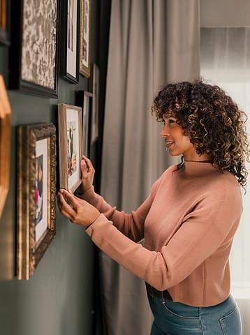 A woman hangs pictures in frames on a green wall inside her modern manufactured home.