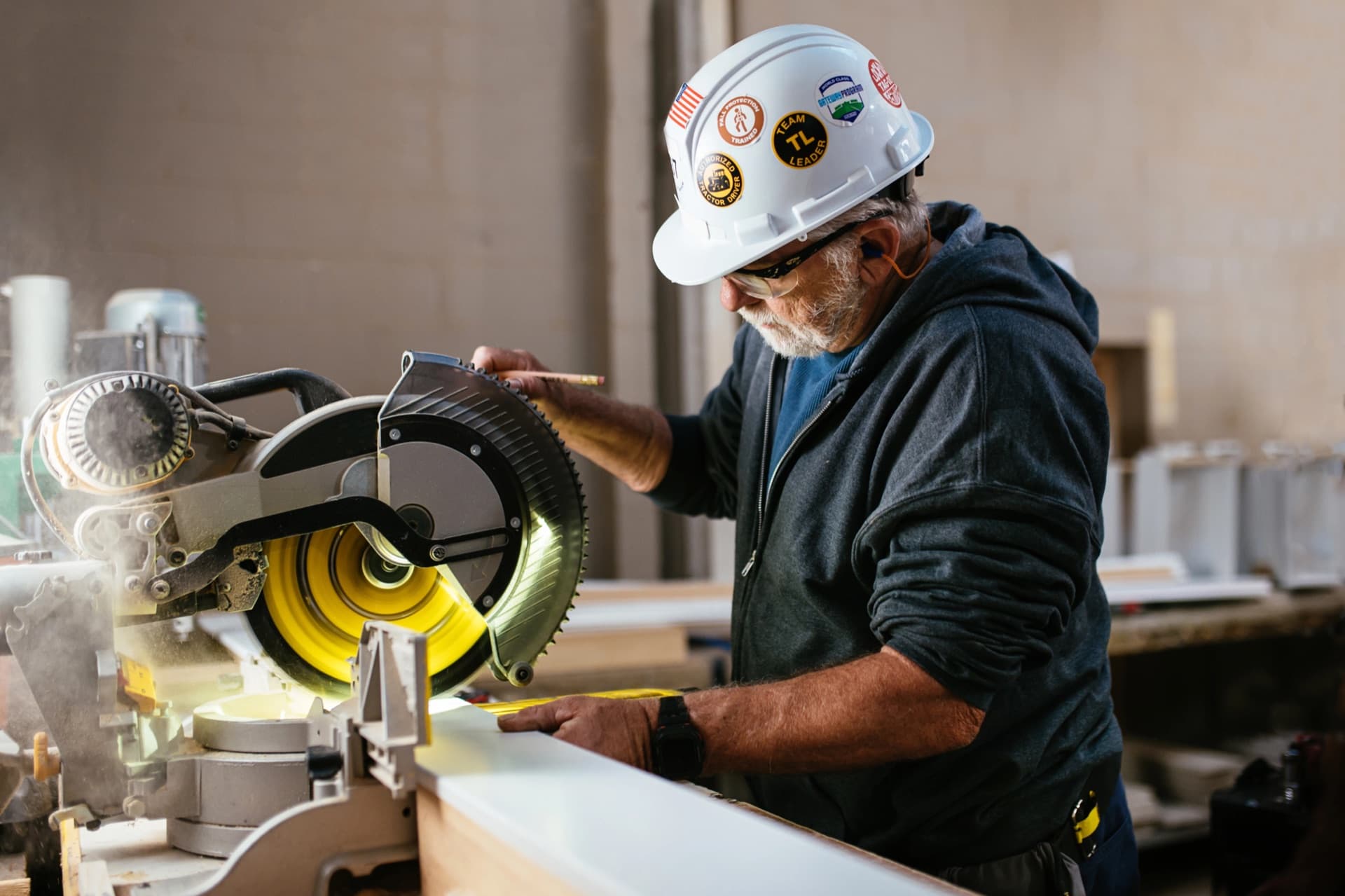 A worker in a hard hat operates a miter saw inside a Clayton home-building facility.