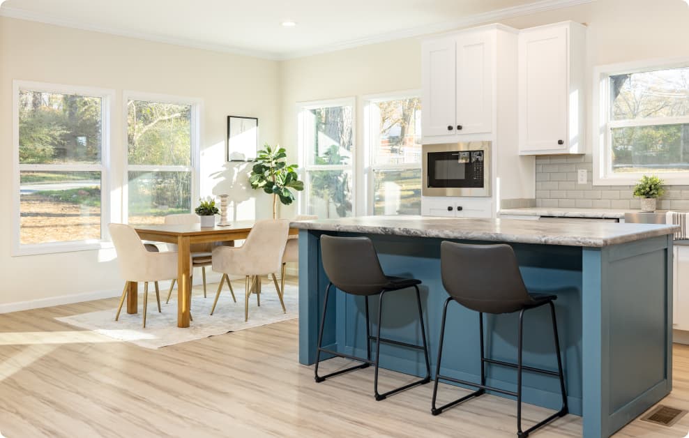 A bright kitchen with blue kitchen island, formal dining room, and white kitchen cabinets with microwave.